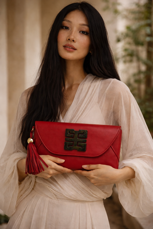 Woman holding a red clutch with a decorative clasp in an outdoor setting
